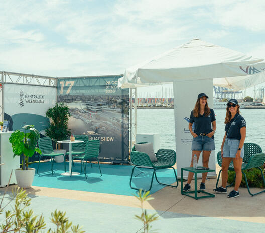 Two team members at the Valencia Boat Show stand, with branded displays, seating and plants beside the marina.