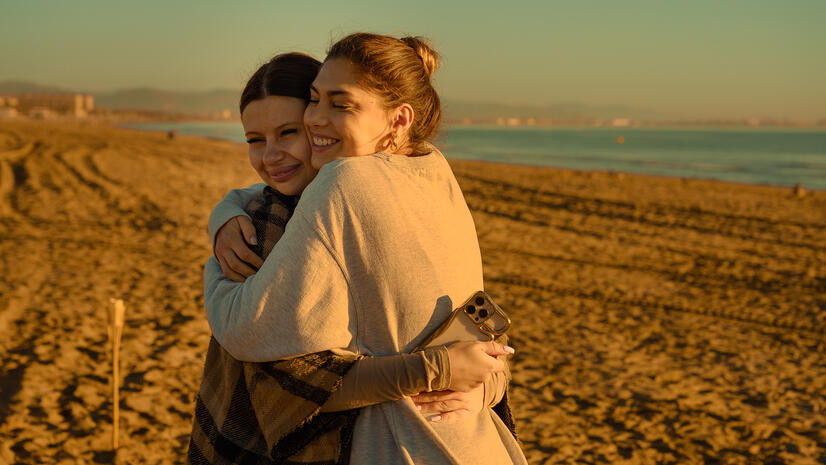 Two women embracing on the beach in warm early-morning light