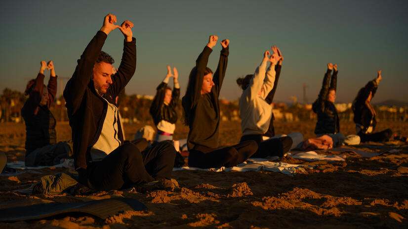 Shared movement at sunrise — Sync Club Group of participants raising their arms together during a sunrise beach session
