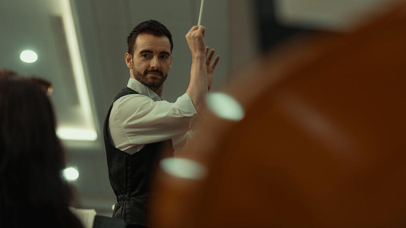 Orchestra conductor raising his baton while leading musicians during a rehearsal