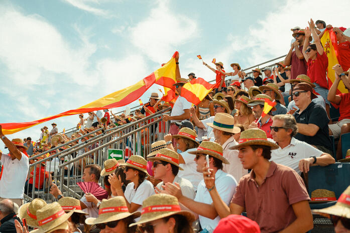 Spectators cheering and waving Spanish flags in packed grandstands at SailGP in Valencia.