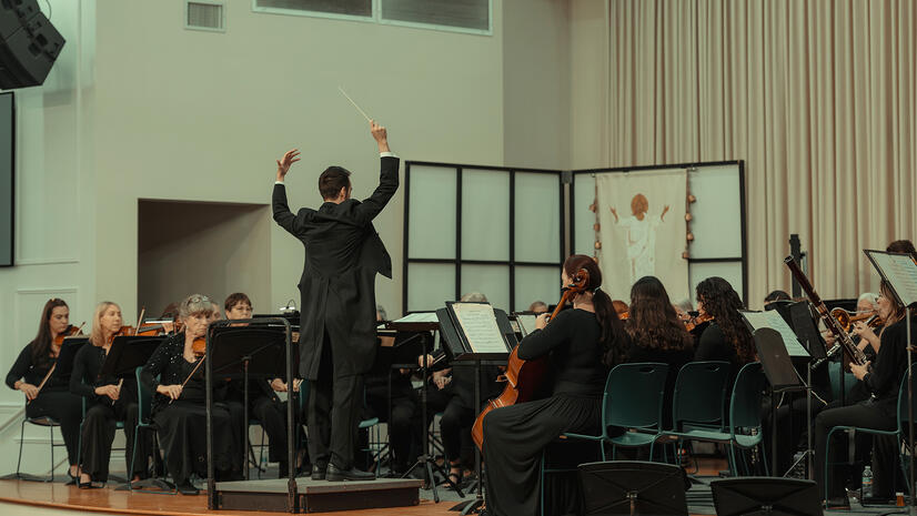 Conductor leading a seated orchestra during a full ensemble rehearsal