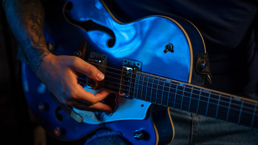 Close view of a musician’s hand playing a blue electric guitar in studio light
