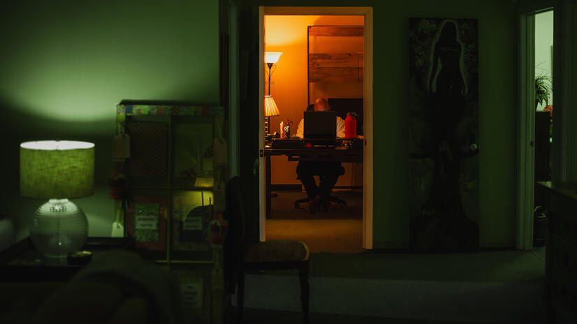 Work after hours Man working at a laptop in a warmly lit office, seen through a doorway from a dark green room