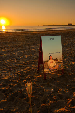 Sync Club event sign standing on a beach in warm sunrise light