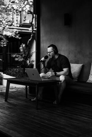 Man wearing headphones and speaking into a microphone while working on a laptop outdoors
