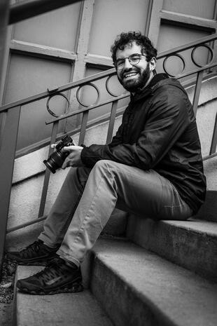 Smiling photographer seated on outdoor steps and holding a professional camera