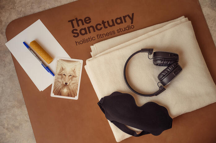 Branded Sanctuary fitness studio mat arranged with headphones, a blanket, an eye mask and printed materials