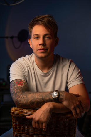 Relaxed professional portrait Tattooed man in a white T-shirt seated against a dark blue background