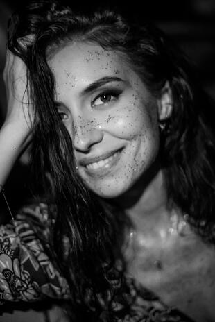 Close black-and-white portrait of a smiling woman with dark hair and freckles