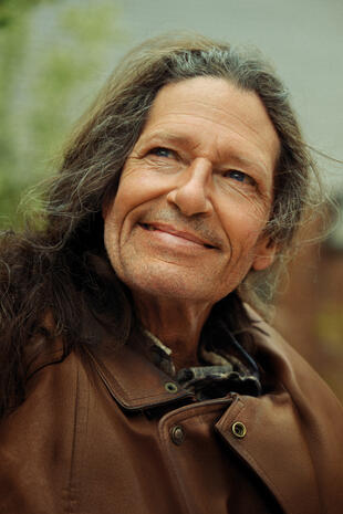 Close outdoor portrait of an older man with long hair and a gentle smile