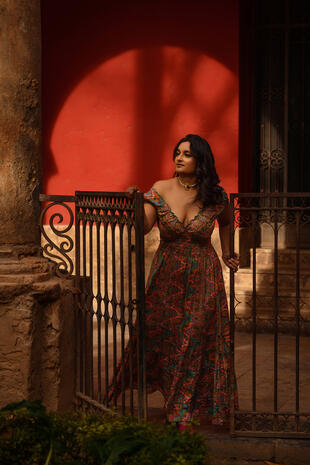Woman in a floral dress standing beside a metal gate and a warmly lit wall at night