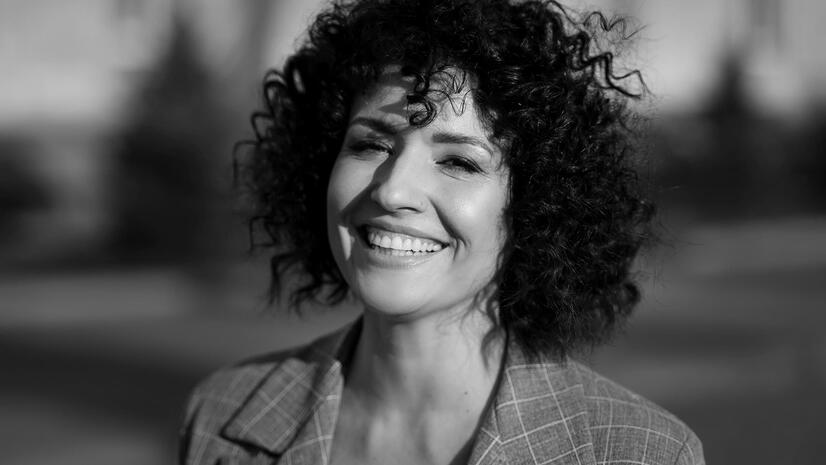 Smiling woman with short curly hair wearing a checked blazer in a black-and-white portrait