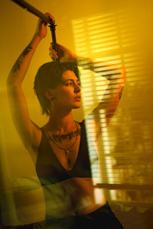 Woman with one arm raised, photographed through layered golden light and reflections