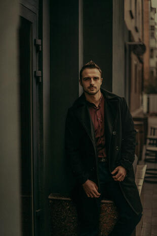 Man in a dark coat standing in a narrow shadowed passage between city buildings