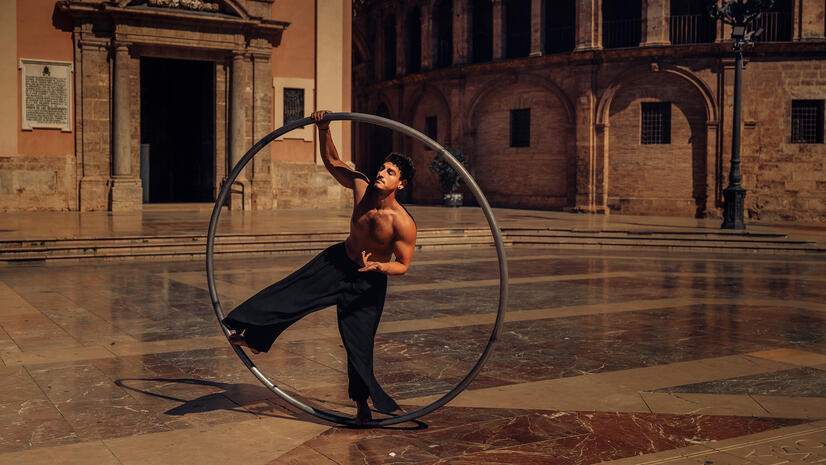 Circus performer balancing inside a large metal Cyr wheel in a historic city square