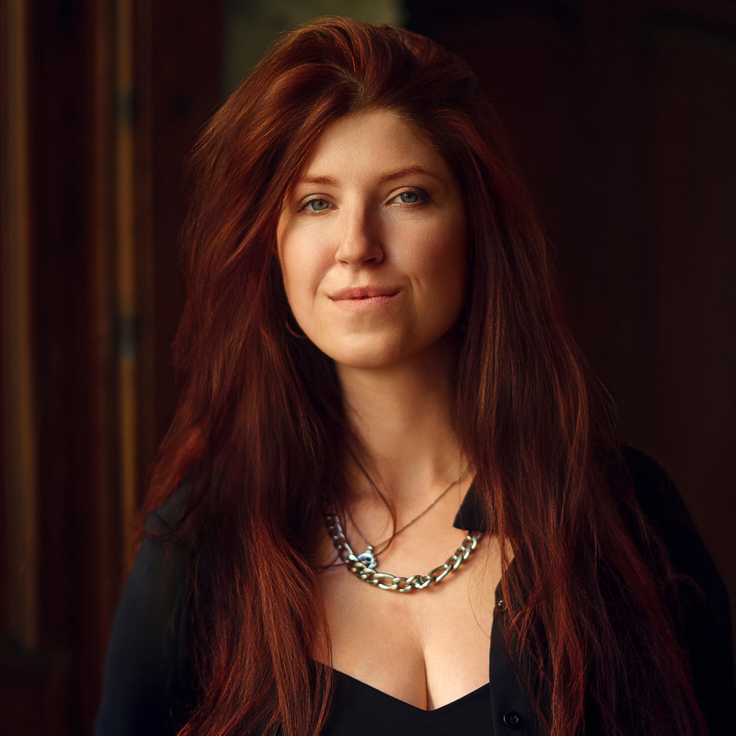 Portrait of photographer Alisa Zenkina with long red hair, wearing black and looking directly at the camera