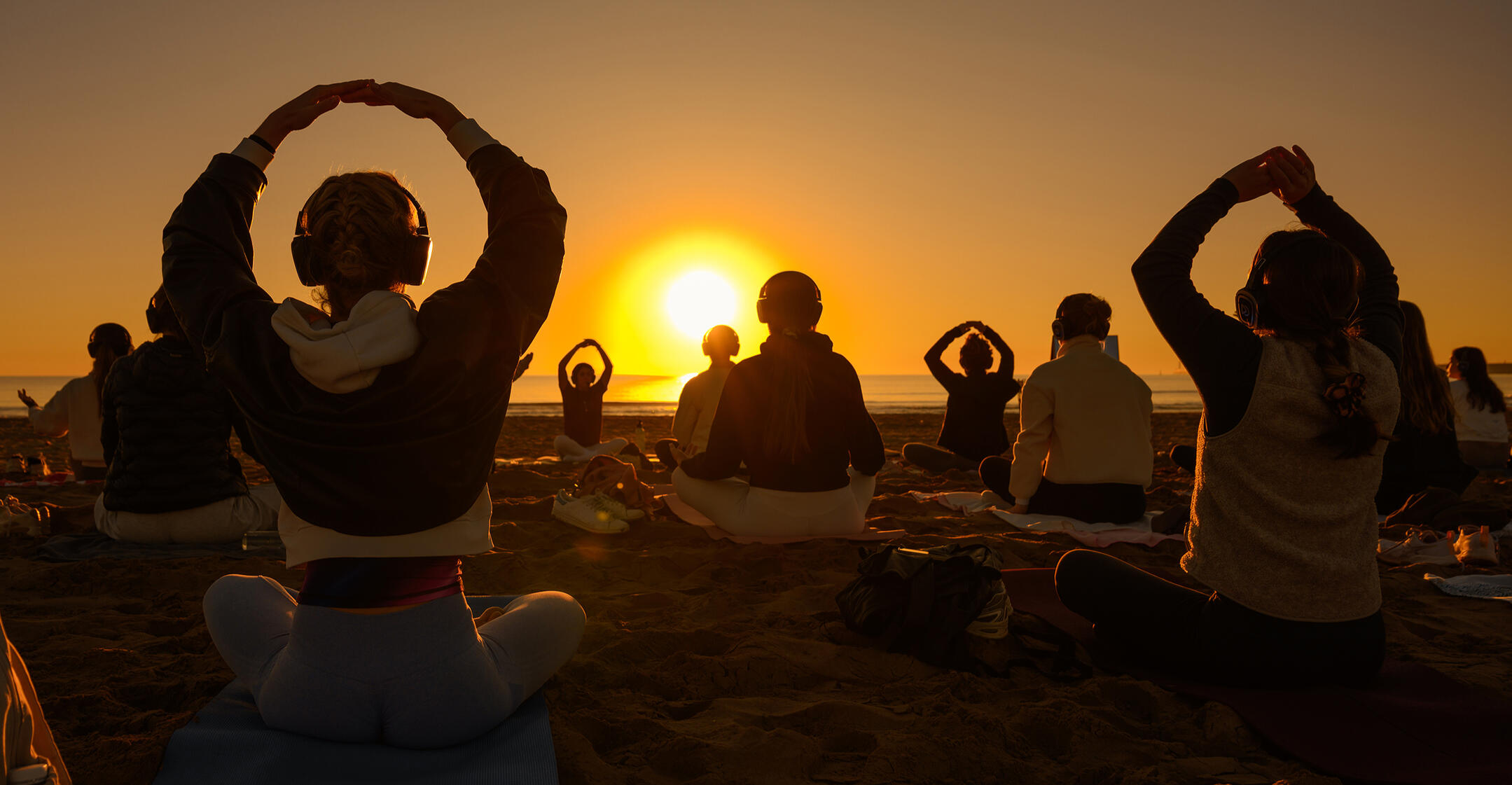 Group breathwork session on a beach at sunrise, with participants seated around the rising sun