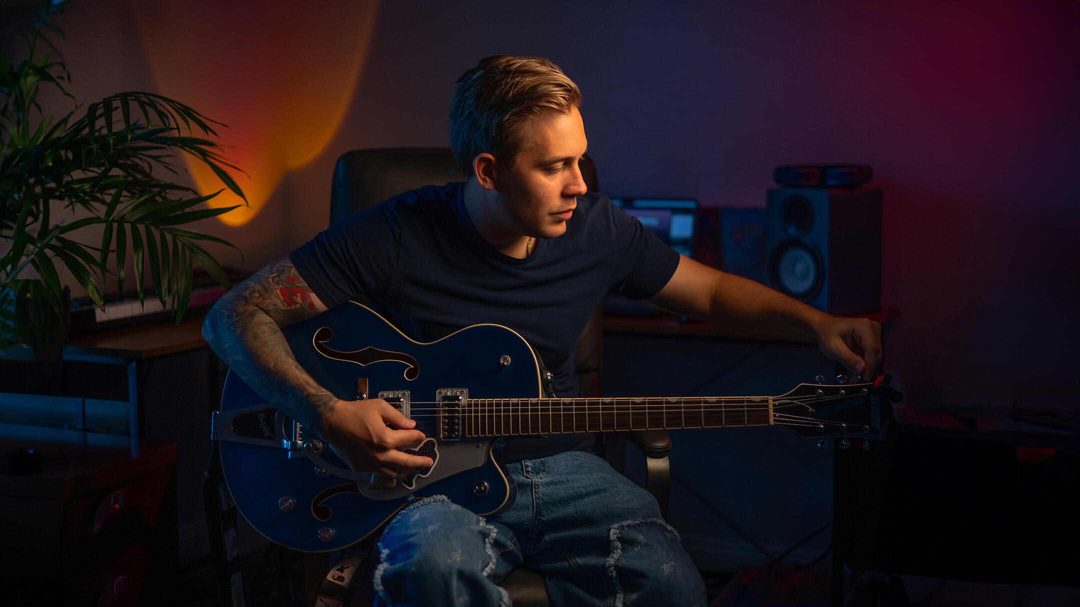 Musician in his creative workspace Musician seated with an electric guitar in a recording studio lit with blue and magenta light